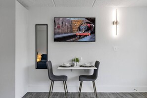 Een moderne eetruimte met een televisie aan de muur waarop een trein te zien is, twee stoelen, een klein tafeltje met borden en een spiegel.