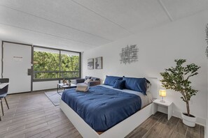 Een moderne slaapkamer met een groot bed, een bureau en een balkon met uitzicht op bomen.