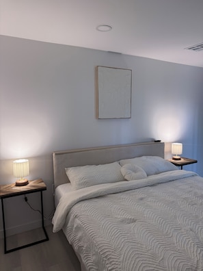 A bedroom with a bed, two bedside tables with lamps, a radiator, and a framed picture on the wall.