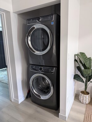 A stacked washer and dryer unit in a modern kitchen with a potted plant beside it.