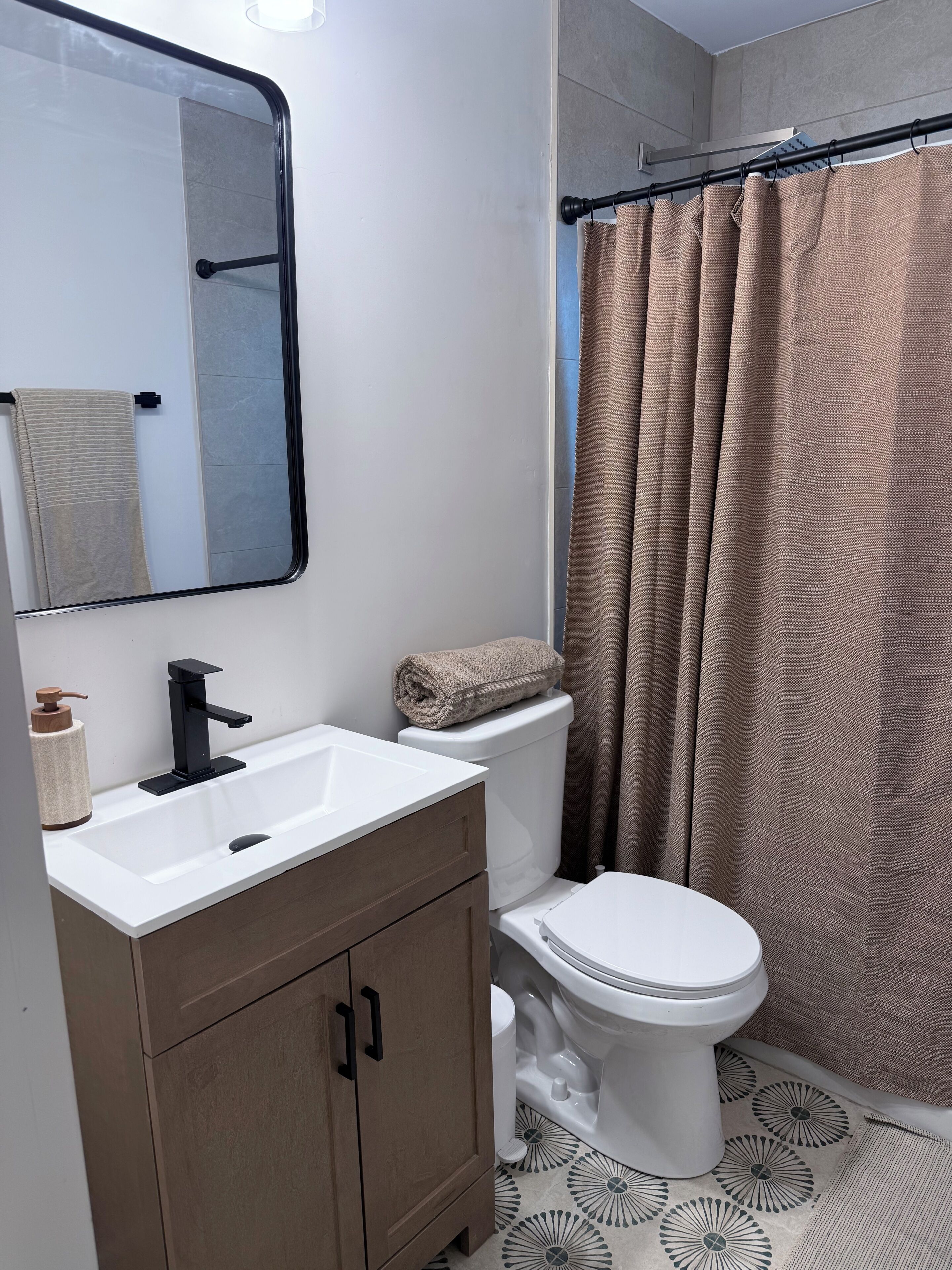 A bathroom with a white sink, black faucet, wooden cabinet, white toilet, and a shower curtain.