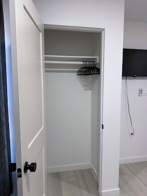 A room with a white door, a black door handle, a white closet with a black hanger rack, a flat-screen TV mounted on the wall, and a power outlet. - Modern 3BD Central Phoenix Home (Phoenix)