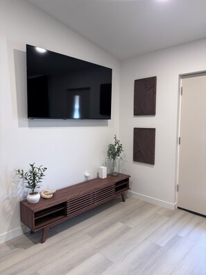 Un salon moderne avec un téléviseur à écran plat fixé au mur, une console en bois agrémentée d’objets décoratifs et une porte fermée.
