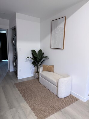 A modern living room with a sofa, a large potted plant, a framed artwork on the wall, and a washing machine in the background. - Modern 3BD Central Phoenix Home (Phoenix)