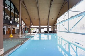 An indoor swimming pool with clear water, a lifeguard stand, and a seating area with chairs. - Cozy Spacious Resort Suite With Kitchen and Living Room (Oro-Medonte)