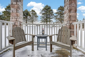 A snow-covered outdoor seating area with two Adirondack chairs and a small table, surrounded by a white fence and stone pillars. - Cozy Spacious Resort Suite With Kitchen and Living Room (Oro-Medonte)