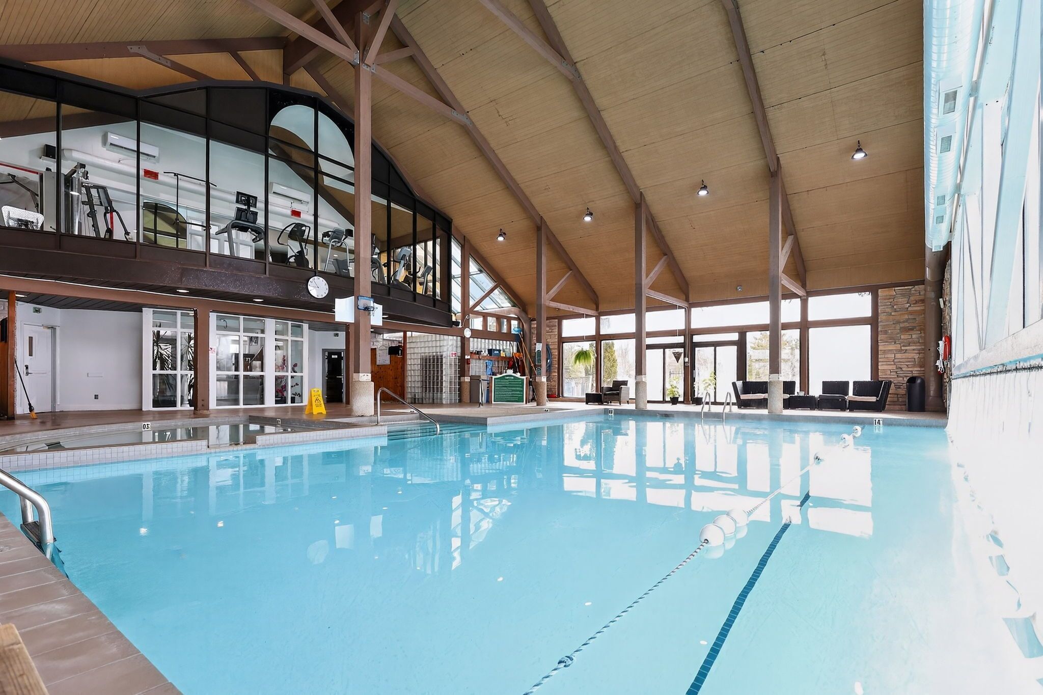 Une piscine intérieure avec des couloirs bien délimités, un plafond en bois et, au fond, du matériel d’exercice.