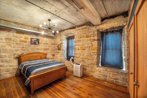 A bedroom with a wooden bed, stone walls, a window with curtains, and a ceiling fan.