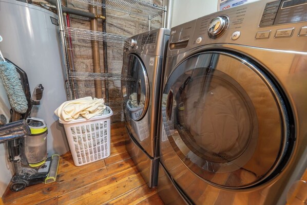 A front-loading washing machine and dryer in a laundry room with a wooden floor.