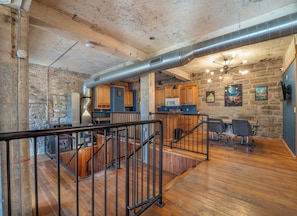 A spacious kitchen with wooden cabinets, a dining area with chairs, and a staircase with a metal railing.