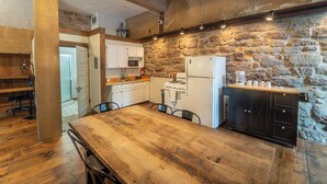 Una cucina rustica con parete in pietra, tavolo di legno e mobili bianchi.