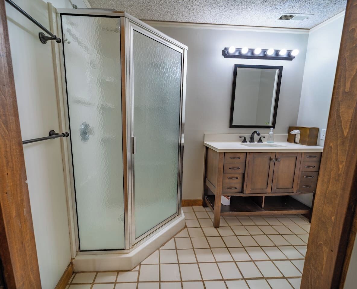 Une salle de bain avec une douche à parois de verre, un meuble-lavabo avec un miroir et un espace coiffeuse éclairé.