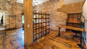A rustic room with exposed stone walls, wooden flooring, a metal rack, and a desk with a chair.