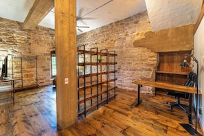 A rustic room with exposed stone walls, wooden flooring, a metal rack, and a desk with a chair. - Charming 1863 Brewery Loft + Underground Caves (Jordan)
