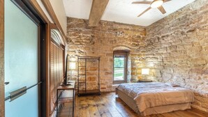 Una camera da letto con pareti in pietra, pavimento in legno, un letto, una scrivania e una finestra.
