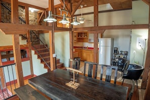 Un comedor amplio con una mesa y sillas de madera, una escalera con barandillas de madera y una cocina al fondo.