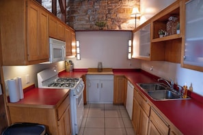 Una cocina compacta con estufa a gas, microondas, gabinetes de madera, encimera roja y pared de piedra.