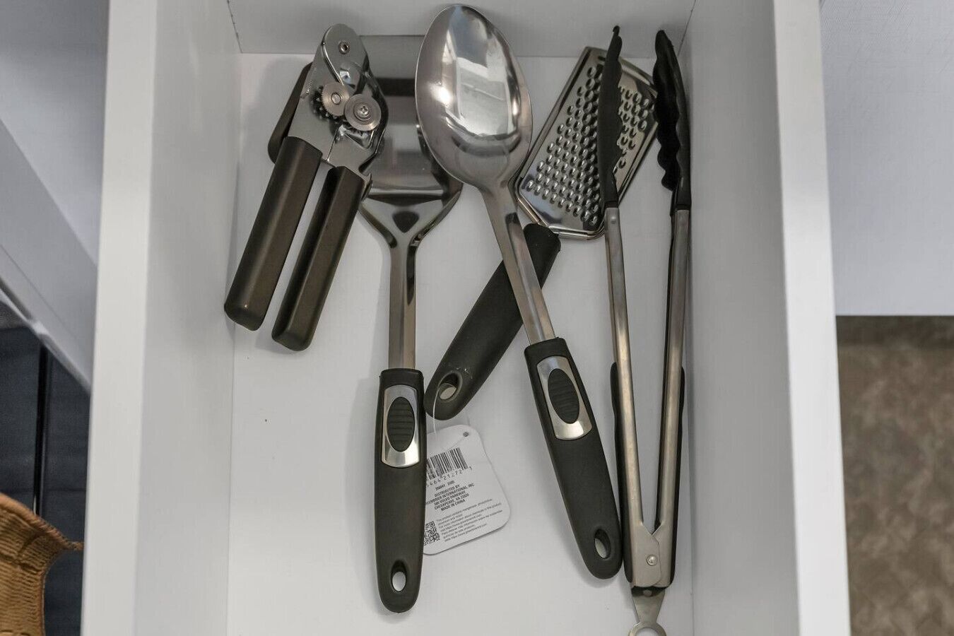 Eine Schublade mit verschiedenen Küchenutensilien, darunter eine Reibe, ein Löffel, ein Messer und eine Schere.
