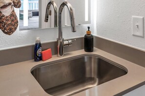 Ett modernt kök med en diskho i rostfritt stål, en blandare, en tvålpump och en flaska diskmedel.