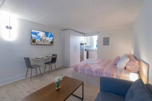 A modern room with a bed, a sofa, a desk, and a chair. There is a painting on the wall and a small table with a vase. - Charming Studio Just 8 Min from Disney | Orl (Kissimmee)