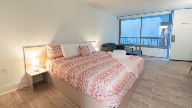 Ett hotellrum med en säng, ett nattduksbord, ett skrivbord och ett stort fönster med utsikt över havet.