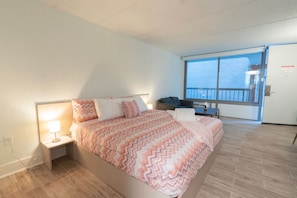 A hotel room with a bed, a nightstand, a desk, and a large window offering a view of the sea. - Charming Studio Just 8 Min from Disney | Orl (Kissimmee)