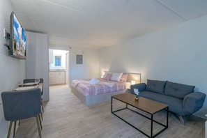 Una habitación de hotel moderna con una cama, un sofá, una mesa de centro y un área de comedor con sillas.