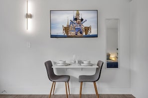 Ein Essbereich mit einem Tisch für zwei Personen, einem darüber hängenden Fernseher und einem Spiegel, der einen Teil des Raumes widerspiegelt.