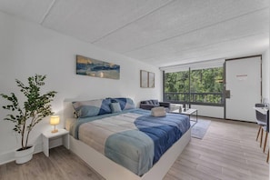 Un dormitorio moderno con una cama grande, mesitas de noche, un escritorio y una ventana con vistas a zonas verdes.