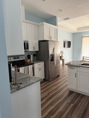 A modern kitchen with white cabinets, a stainless steel refrigerator, a microwave, and a granite countertop.