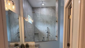 Une salle de bain dotée d’une douche à paroi de verre, d’un lavabo avec un plan de travail en granit et d’un grand miroir.