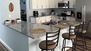 A modern kitchen with white cabinets, a central island with bar stools, and stainless steel appliances.
