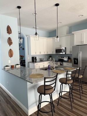 A modern kitchen with white cabinets, a central island with bar stools, and stainless steel appliances.