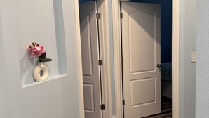 A hallway with two white doors, a small vase with flowers, and a light switch on the wall.