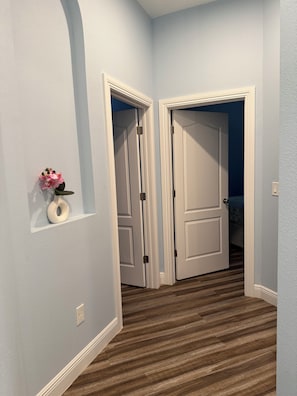 A hallway with two white doors, a small vase with flowers, and a light switch on the wall.