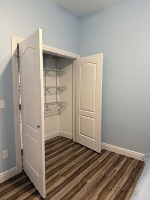A room with a wooden floor, a white door, and a closet with shelves.