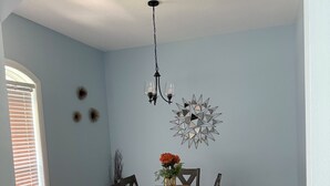 Un coin repas avec une table dressée pour quatre personnes, des chaises en bois, un lustre et des œuvres d’art décoratives accrochées au mur.
