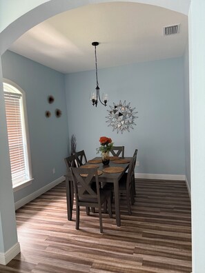 A dining area with a table set for four, wooden chairs, a chandelier, and decorative wall art. - Furnished 3 bedroom, easy I-4 Access (Plant City)