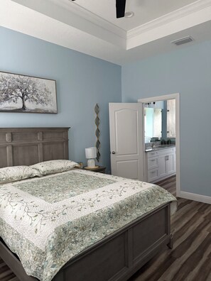 A bedroom with a bed, a nightstand, a dresser, and a door leading to a bathroom.