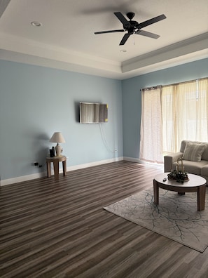 A living room with a ceiling fan, a mounted TV, a sofa, a coffee table, and a lamp.