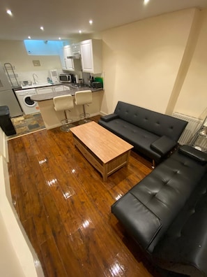 A compact living space with a kitchenette, a black leather sofa, a wooden coffee table, and a small bar stool. - Perfect 3-bedroom apartment in charming Edinburgh close to city center (Edinburgh)