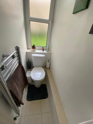 A small, narrow bathroom with a toilet, a radiator, a towel rack, and a window with a view of greenery. - Perfect 3-bedroom apartment in charming Edinburgh close to city center (Edinburgh)