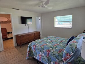 Een slaapkamer met een bed, een kaptafel, een plafondventilator en een raam.
