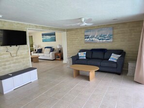 Ein Wohnzimmer mit grauem Sofa, einem Holztisch, einem flachbildfernseher an der Wand und einem Gemälde eines Segelboots an der Wand.
