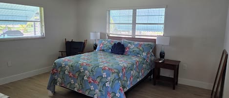 Ein Schlafzimmer mit einem Bett, zwei Nachttischen, einem Deckenventilator und zwei Fenstern mit Jalousien.