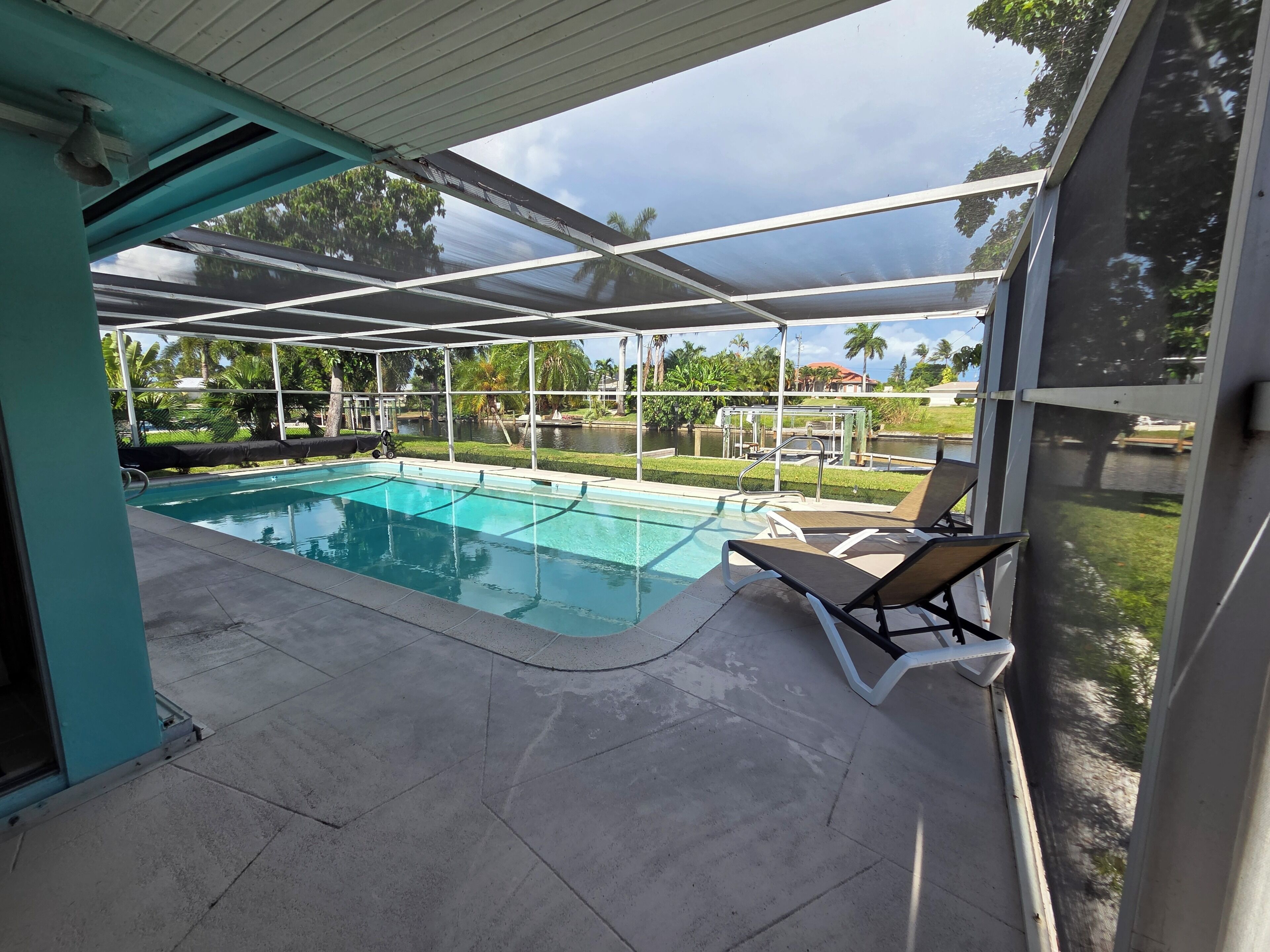 A covered swimming pool with lounge chairs and a view of a landscaped area.