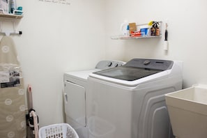 A laundry room with a front-loading washing machine, a drying rack, and a shelf with cleaning supplies.