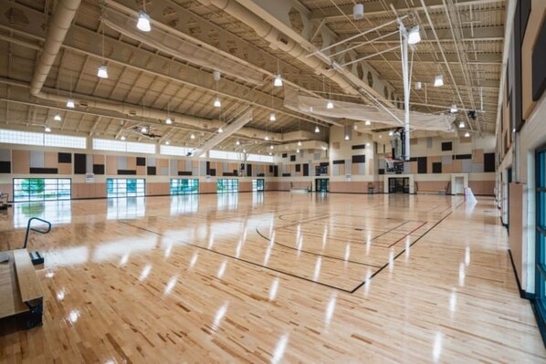 A spacious indoor area with a polished wooden floor, high ceilings with exposed ductwork, and large windows allowing natural light.
