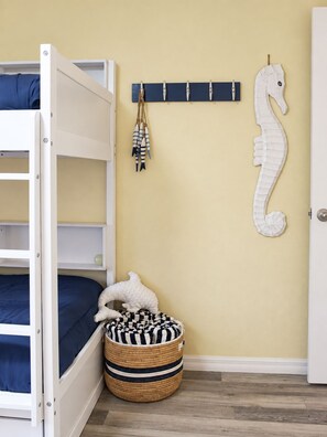 A bunk bed with a headboard, a wall-mounted coat rack with keys, a seahorse decoration, a woven basket with a plush toy, and a door.