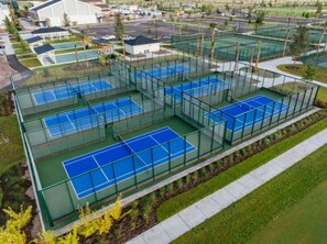 A sports complex with multiple tennis courts enclosed by green fencing.
